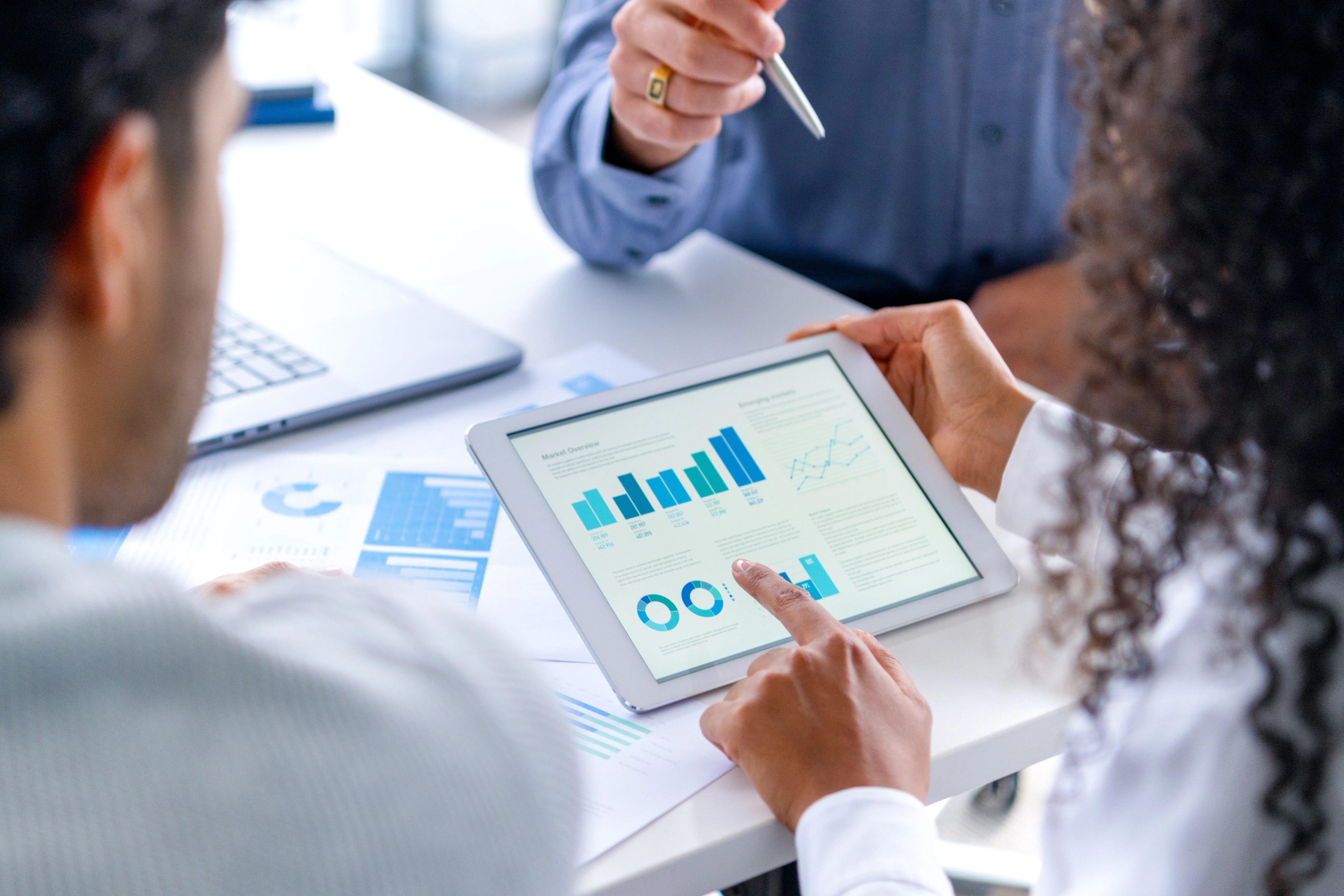 Close up of three people looking at financial data with graphs and charts.